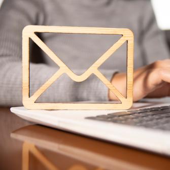 Kuvituskuva, jossa kannettavan tietokoneen kirjoitusosan vierellä puusta tehty sähköpostikuvaketta muistuttava esine.
