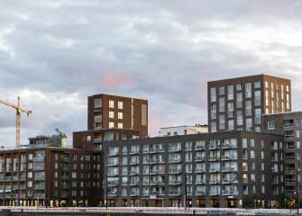 Uusia kerrostaloja ja rakennustyömaa nostokurkineen kaupunkimaisemassa iltavalossa.