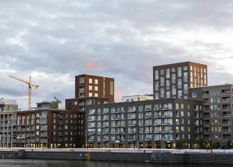 Uusia kerrostaloja ja rakennustyömaa nostokurkineen kaupunkimaisemassa iltavalossa.