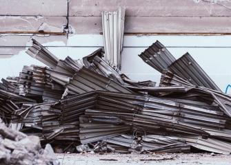 Kasa talon katolta purettua peltikattoa maassa seinän vieressä.