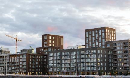 Uusia kerrostaloja ja rakennustyömaa nostokurkineen kaupunkimaisemassa iltavalossa.