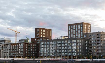 Uusia kerrostaloja ja rakennustyömaa nostokurkineen kaupunkimaisemassa iltavalossa.