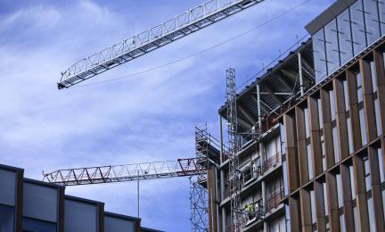 Rakennustyömaa, jossa kaksi torninosturia ja keskeneräinen monikerroksinen rakennus.